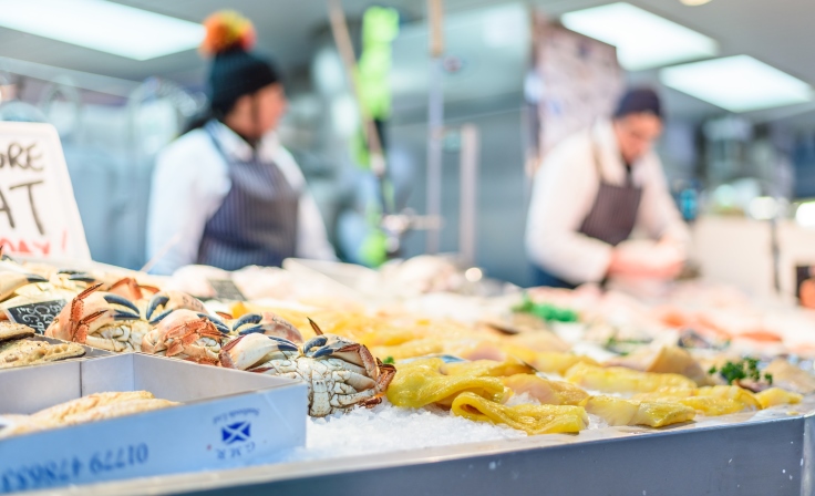 A display of produce, with stall holders preparing food in the background